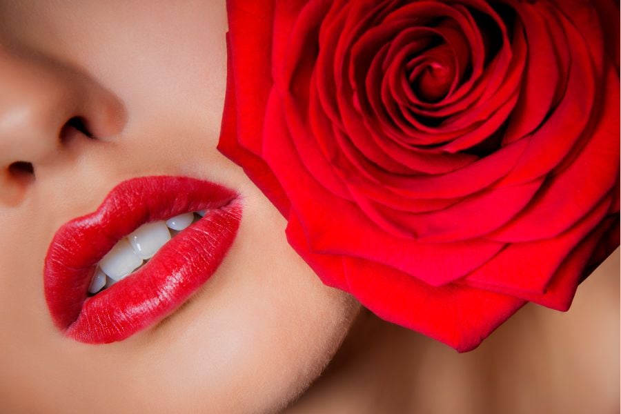 Cận cảnh đôi môi đỏ và bông hồng đỏ tươi ở cạnh, tạo điểm nhấn nổi bật và quyến rũ.