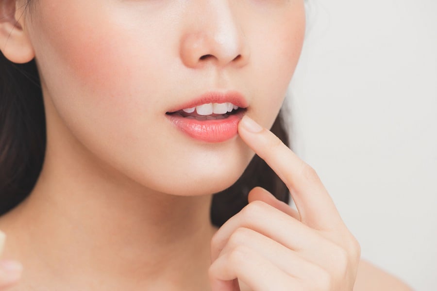 Người chạm tay lên môi, cận cảnh khuôn mặt với nền trắng.