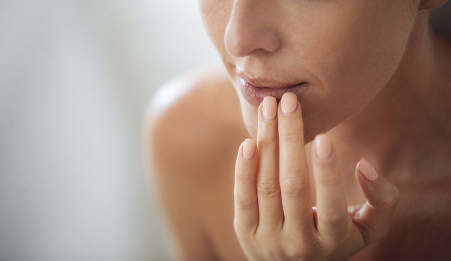 Người chạm nhẹ vào môi bằng ngón tay, với móng tay được sơn màu tự nhiên.