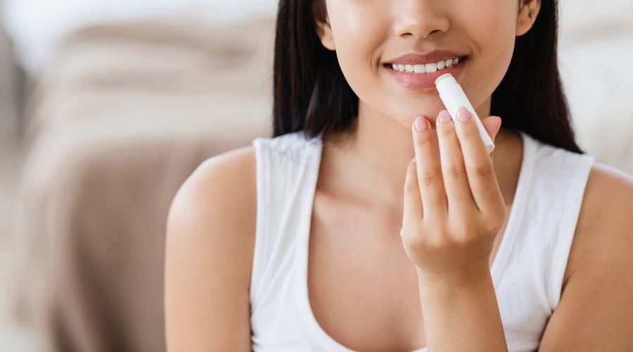 Người đang thoa son dưỡng môi, mặc áo trắng, trong không gian nội thất sáng sủa.