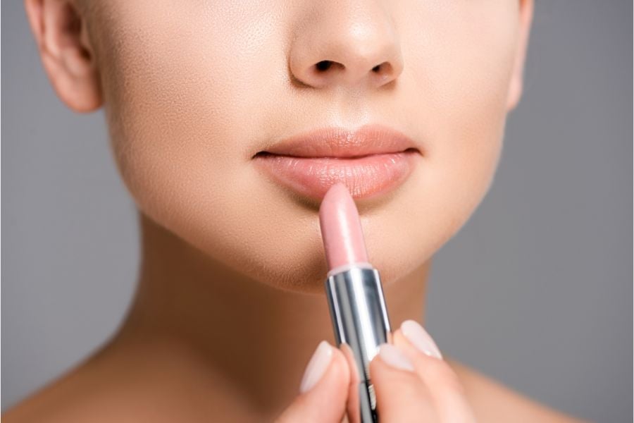 Người đang thoa son màu hồng nhạt lên môi, cận cảnh khuôn mặt và thỏi son.