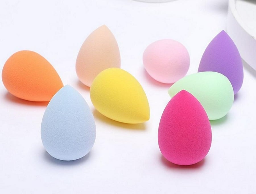 Các miếng bọt biển trang điểm nhiều màu sắc hình giọt nước được xếp trên nền trắng.