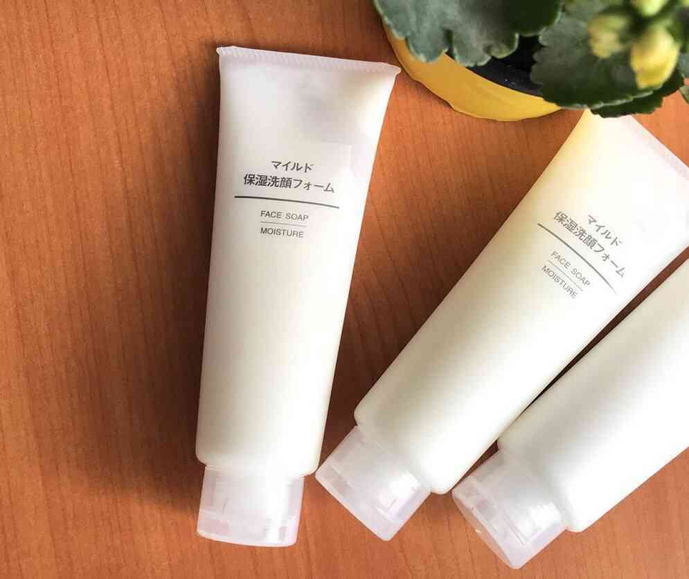 my-pham-muji-3-2 Ba tuýp sữa rửa mặt trên bàn gỗ, bên cạnh chậu cây nhỏ màu vàng.