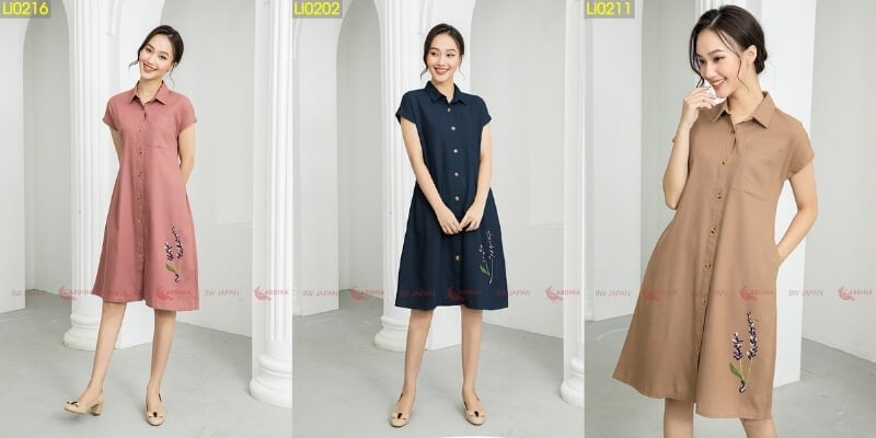 Ba người mẫu mặc váy liền thân có thêu hoa, đứng tạo dáng trước cột trắng trong phòng.