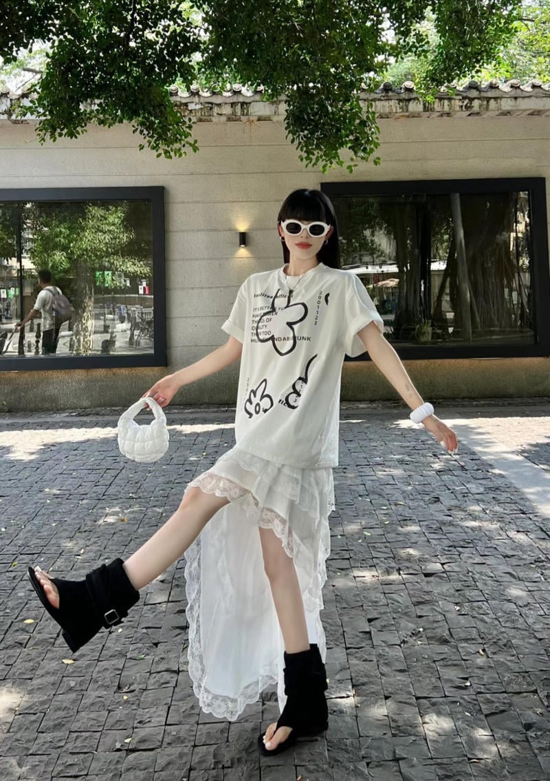 Người đang tạo dáng trong trang phục thời trang với áo thun và váy ren, đeo kính mát, đứng dưới bóng cây.