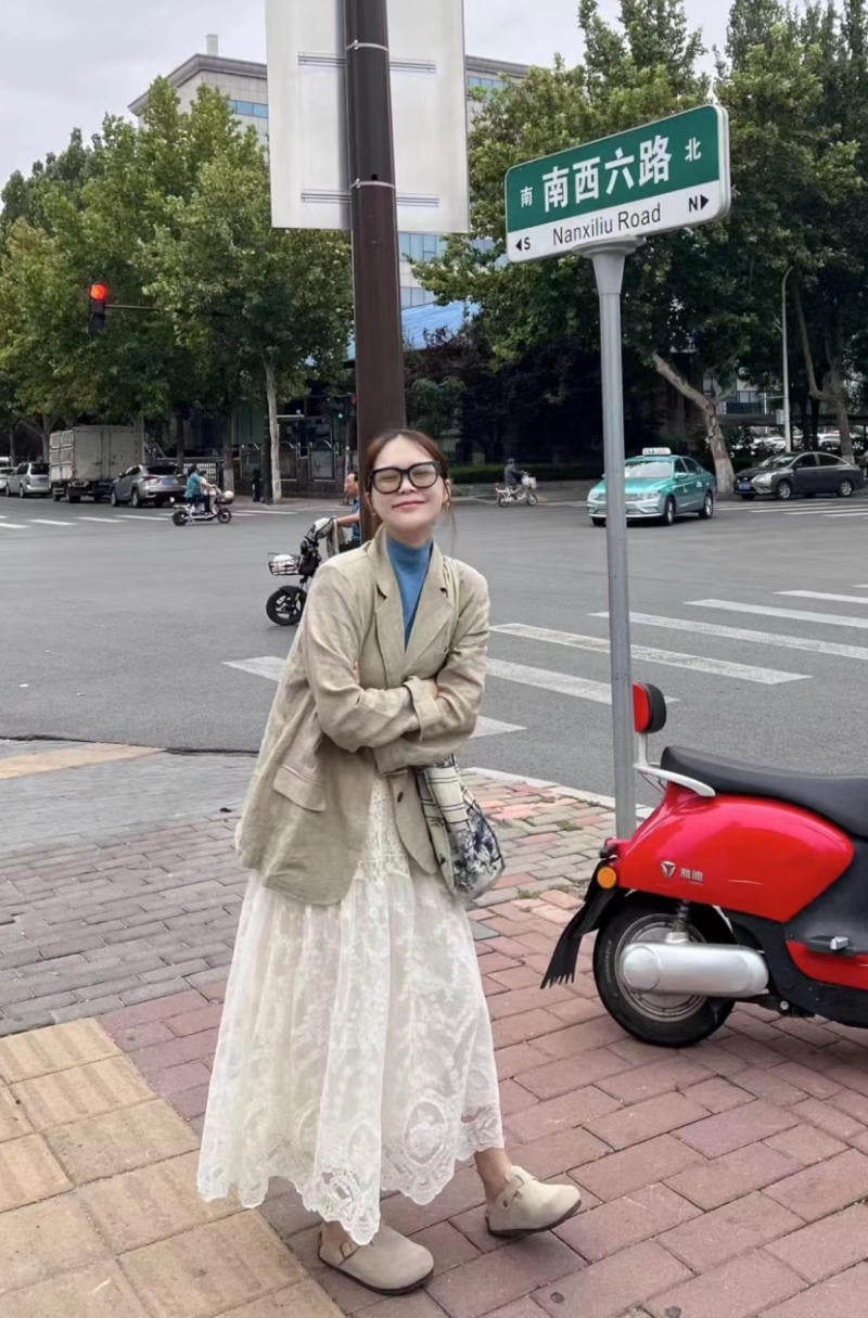 Người đứng trên vỉa hè cạnh biển chỉ đường Nanxilu Road, phía sau là xe mô tô đỏ và giao lộ.