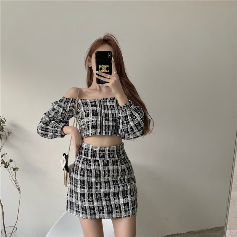 Người mặc áo và váy kẻ caro đen trắng, chụp ảnh tự sướng trước gương, có túi xách nhỏ đeo vai.