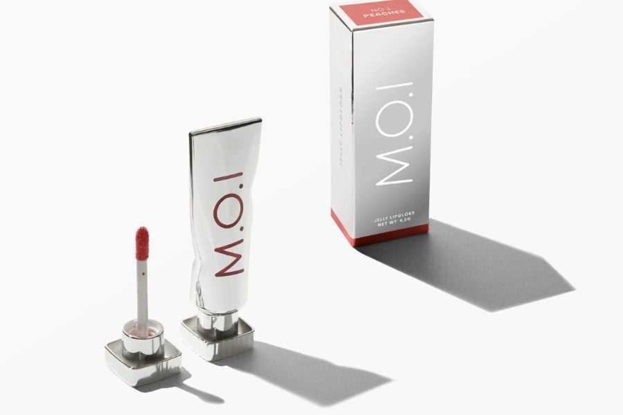 Son bóng dạng tuýp và hộp đựng màu trắng, chữ đỏ, đặt trên nền sáng với bóng đổ nhẹ.