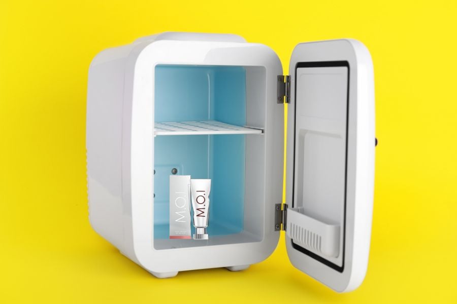 Tủ lạnh mini màu trắng mở cửa, bên trong có sản phẩm mỹ phẩm, nền màu vàng sáng.