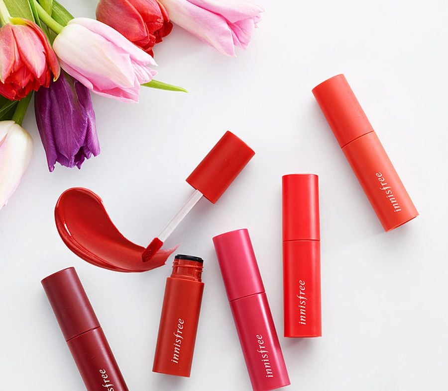 Son môi nhiều màu sắc nằm gần bó hoa tulip trên nền trắng.