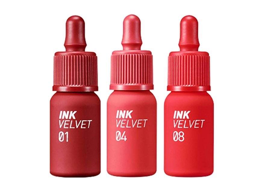 Ba chai son môi màu đỏ với nhãn "INK VELVET" và số hiệu 01, 04, 08, có nắp dạng nhỏ giọt.