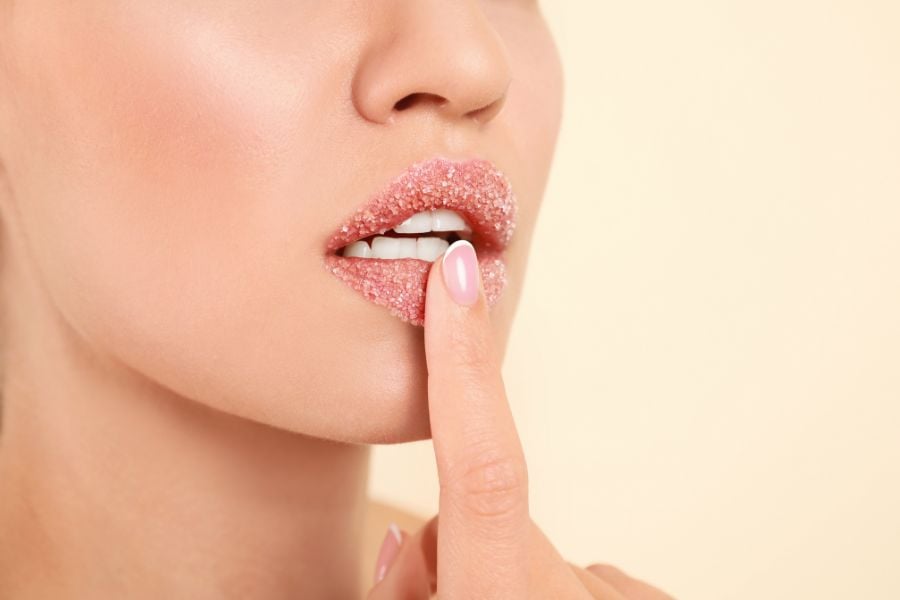 Người chạm vào môi với lớp phủ đường, nền màu be nhạt.