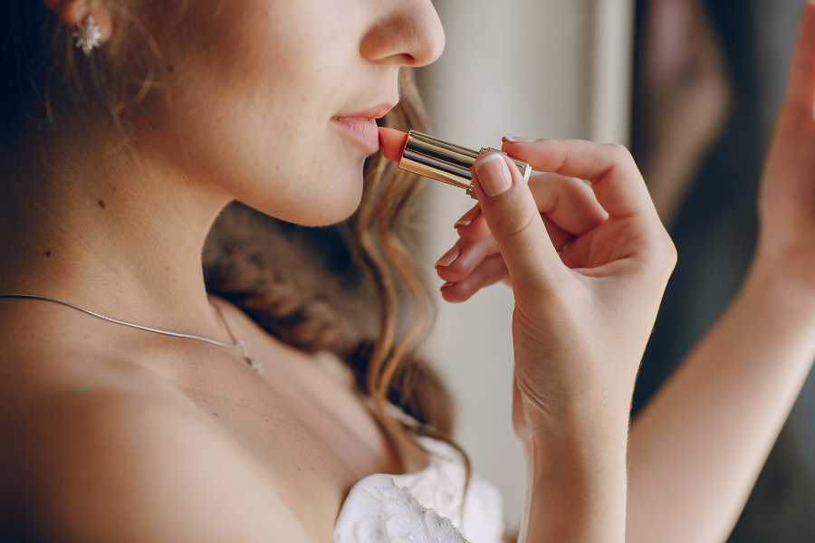 Người phụ nữ đang thoa son môi màu hồng nhạt, đeo bông tai và mặc váy trắng.