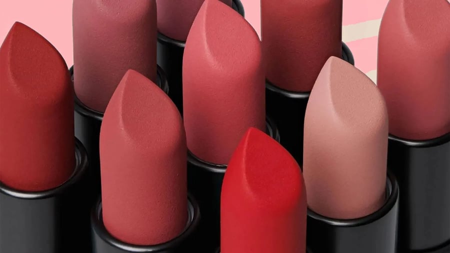 Một nhóm son môi nhiều màu sắc gồm đỏ, hồng và nude, được xếp gần nhau trên nền màu hồng.