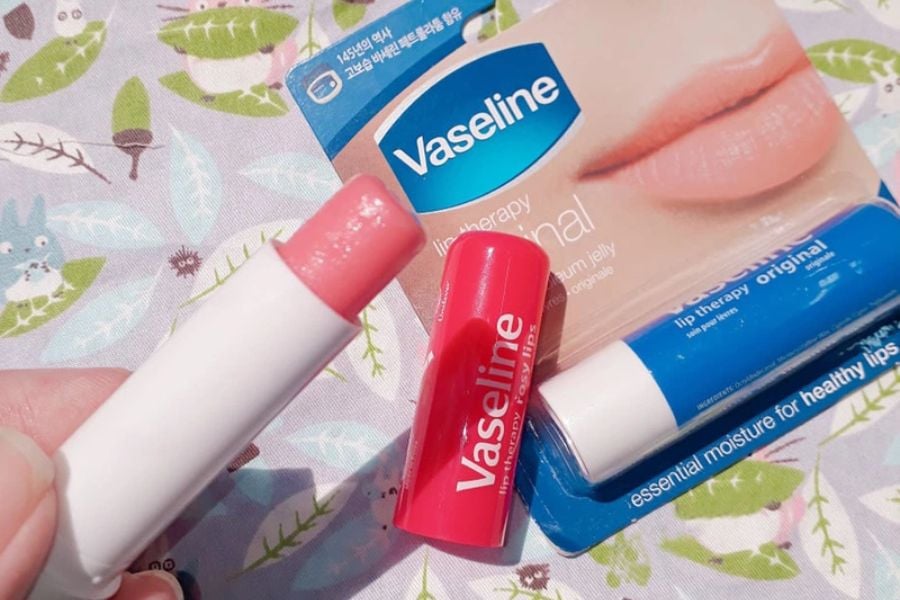 Son dưỡng môi Vaseline màu hồng và xanh, trên nền vải có họa tiết lá và thú hoạt hình.