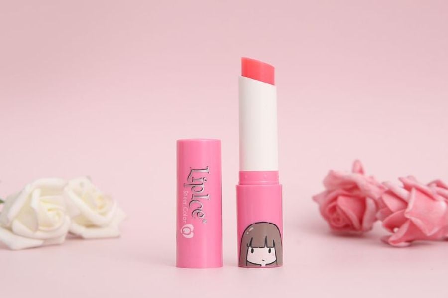Thỏi son dưỡng màu hồng, nắp mở, trên nền hồng, bên cạnh là hoa hồng trang trí.
