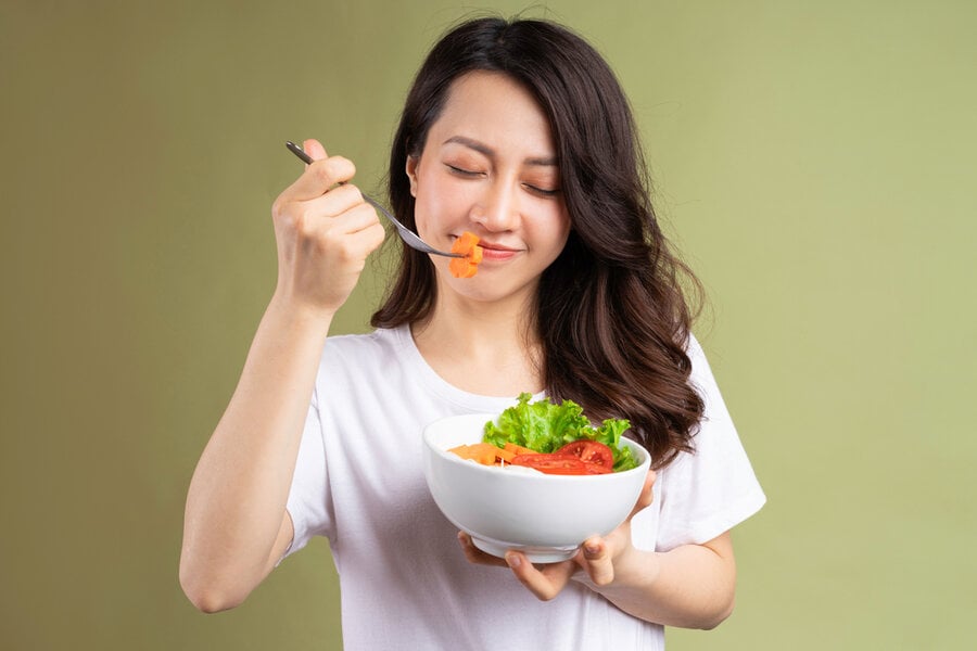 Người cầm tô salad và đưa một miếng cà rốt lên miệng, nền màu xanh lá nhạt.