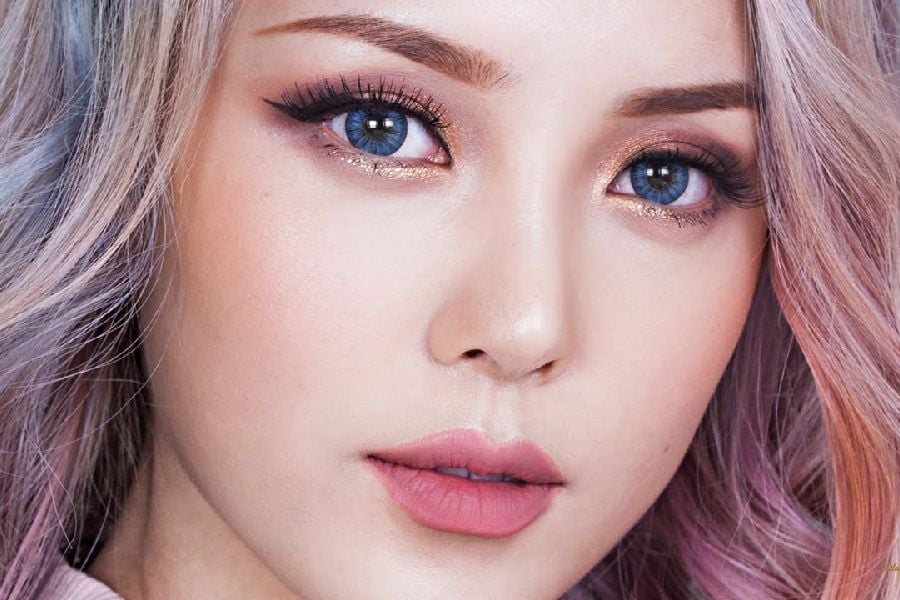 Cận cảnh gương mặt người với tóc nhuộm màu pastel, mắt trang điểm đậm và môi hồng.