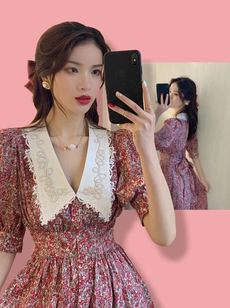 Người phụ nữ chụp ảnh tự sướng trong gương, mặc váy hoa văn đỏ và trắng, nền màu hồng.