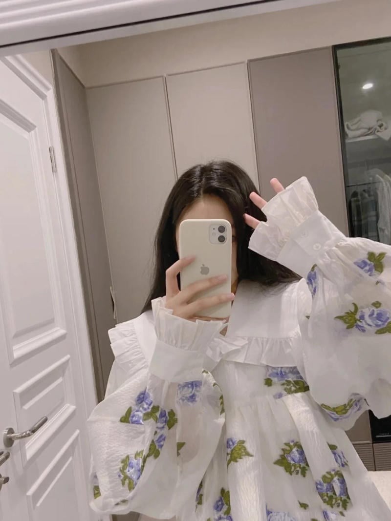 Người mặc áo họa tiết hoa xanh trắng, chụp ảnh tự sướng trước gương trong phòng có cửa tủ.