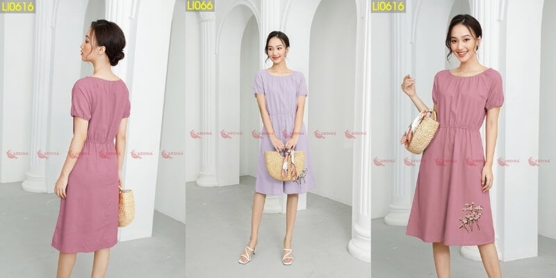 Người mẫu mặc váy màu tím và hồng, tạo dáng bên trong không gian có cột trắng, tay cầm túi xách.