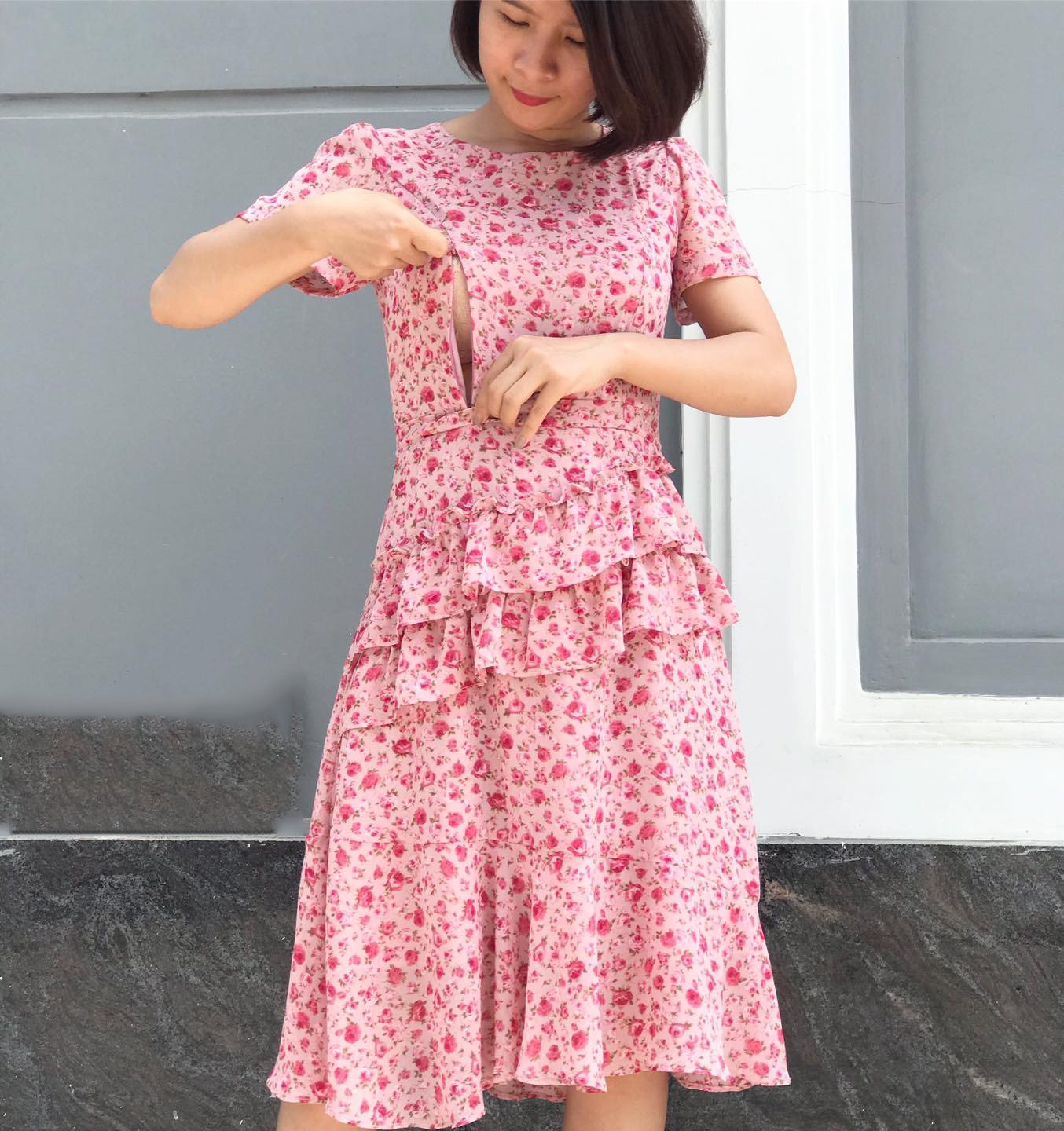 Người phụ nữ mặc váy họa tiết hoa hồng đang kéo khóa bên hông trong môi trường ngoài trời.