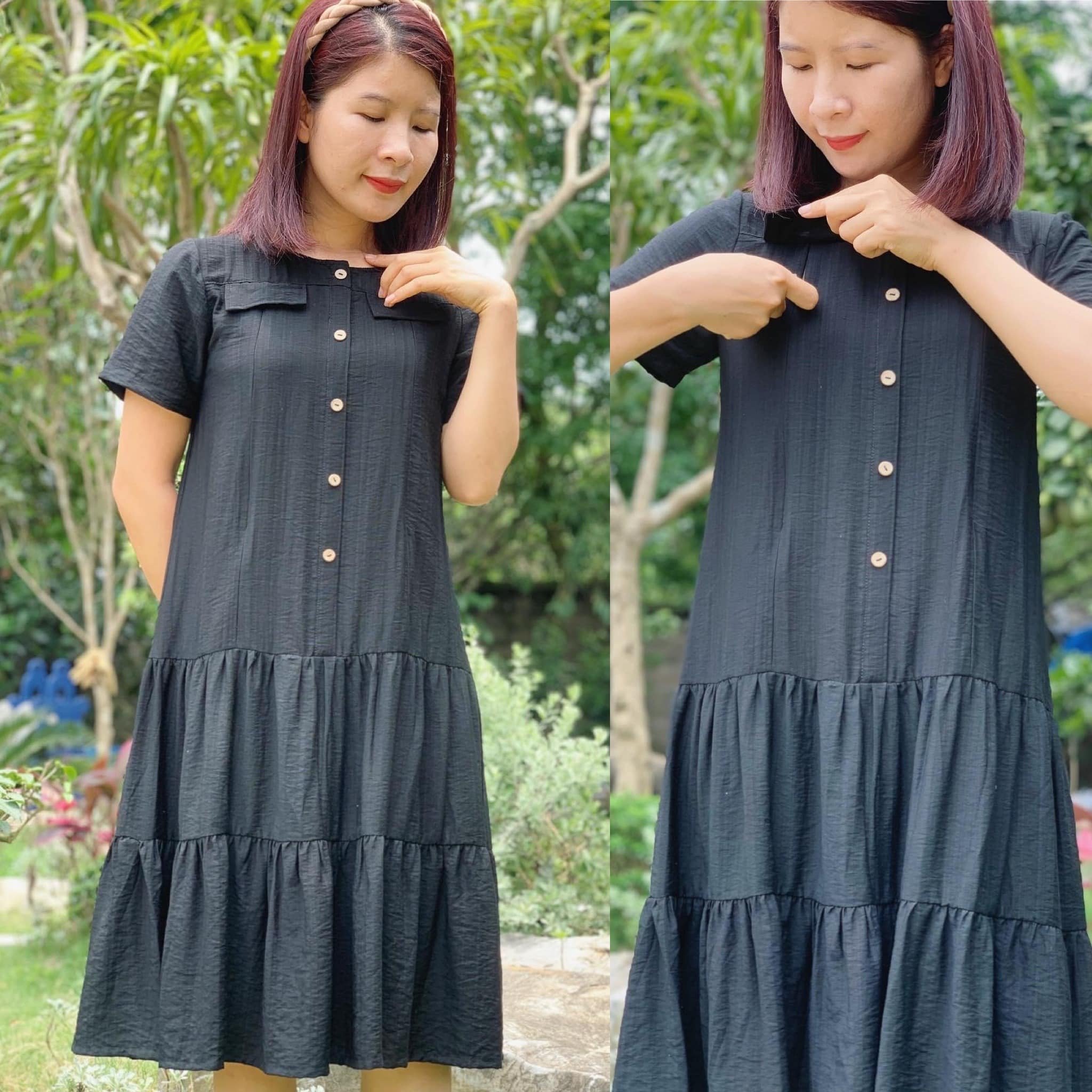 Người phụ nữ mặc váy đen đứng ngoài trời, tay chạm cổ áo, nền là cây xanh.