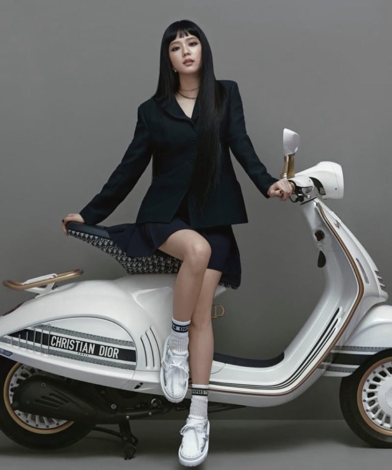 Người mặc trang phục đen ngồi trên xe máy màu trắng có logo thương hiệu thời trang nổi tiếng.