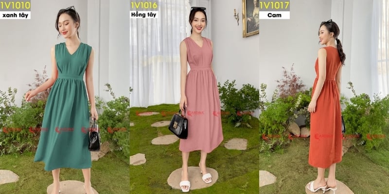Người mẫu mặc váy dài màu xanh, hồng và cam, đứng trong không gian nội thất với cây cối trang trí.