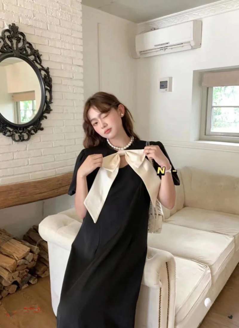 Người mặc váy đen đứng trong phòng khách sáng sủa, có gương và điều hòa trên tường.