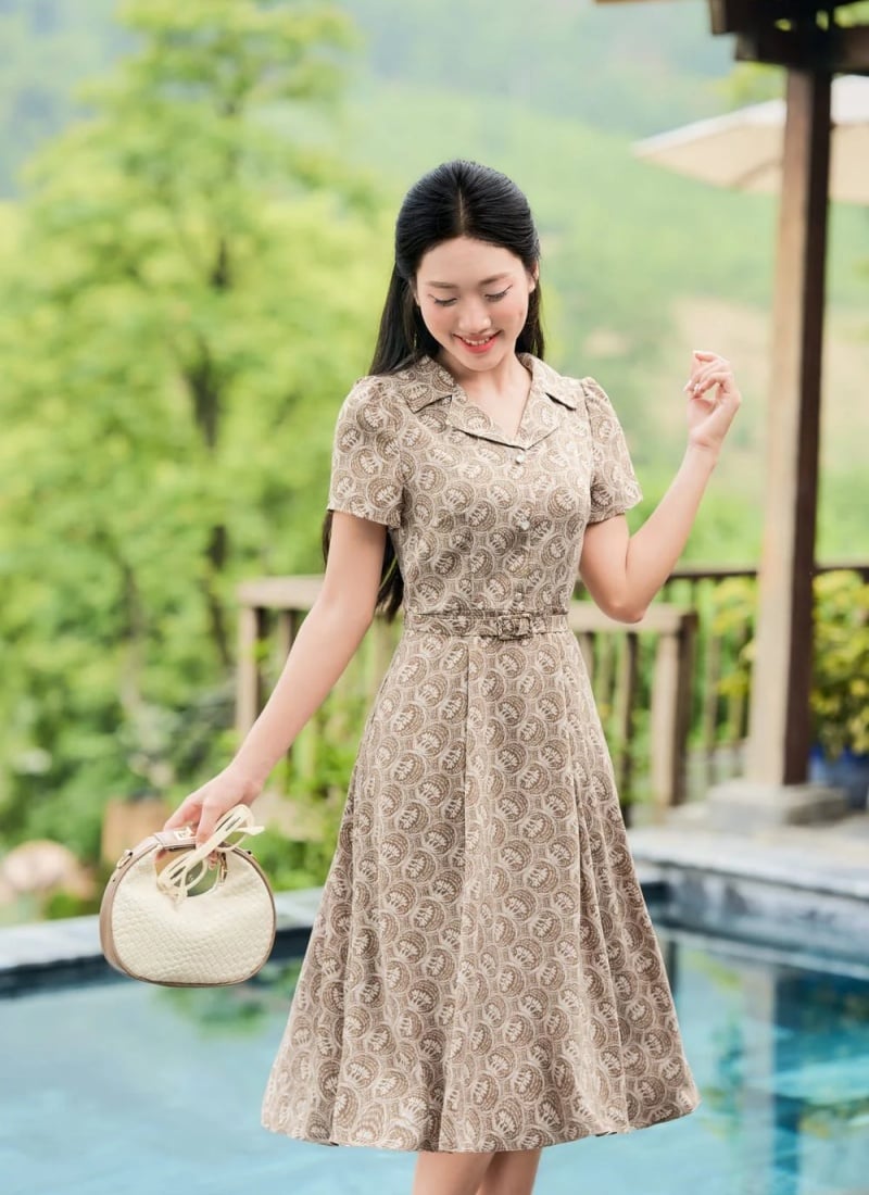 Người phụ nữ mặc váy hoa văn đứng cạnh hồ bơi, cầm túi xách, xung quanh là cây cối xanh tươi.