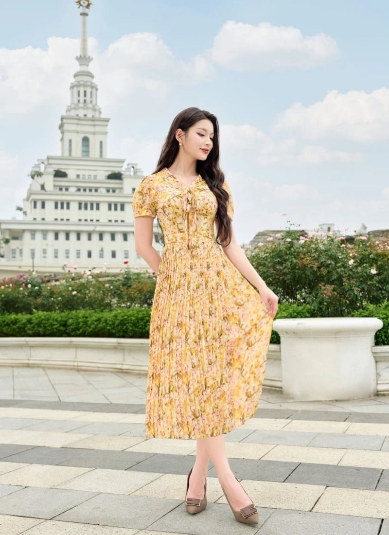 Người mặc váy hoa đứng trước tòa nhà cao tầng, trên nền trời xanh và mây trắng.