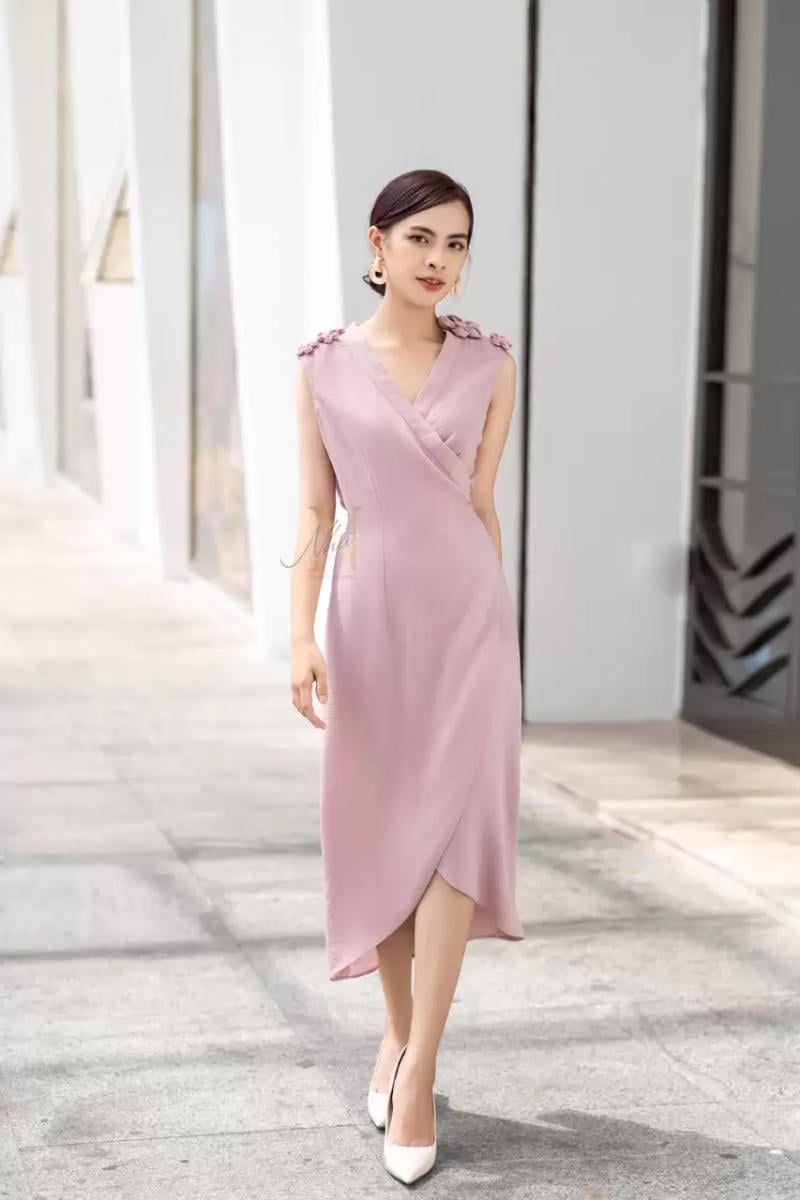 Người phụ nữ mặc váy màu hồng nhạt đứng trên lối đi, nền là kiến trúc hiện đại.