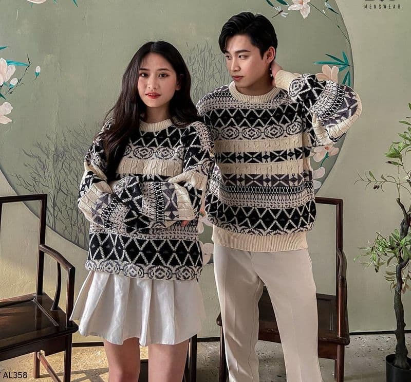 Hai người mặc áo len họa tiết, đứng cạnh nhau, nền hoa văn trang trí, trang phục phối hợp hài hòa.