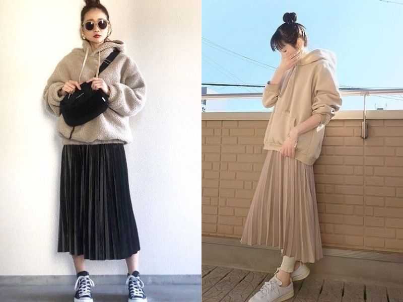 Hai người mặc áo hoodie và váy xếp ly, tạo dáng trước bức tường và ngoài ban công.