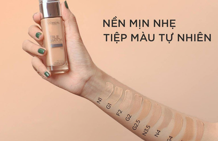 Cánh tay cầm chai kem nền với các tông màu thử khác nhau trên da, nền chữ quảng cáo sản phẩm.
