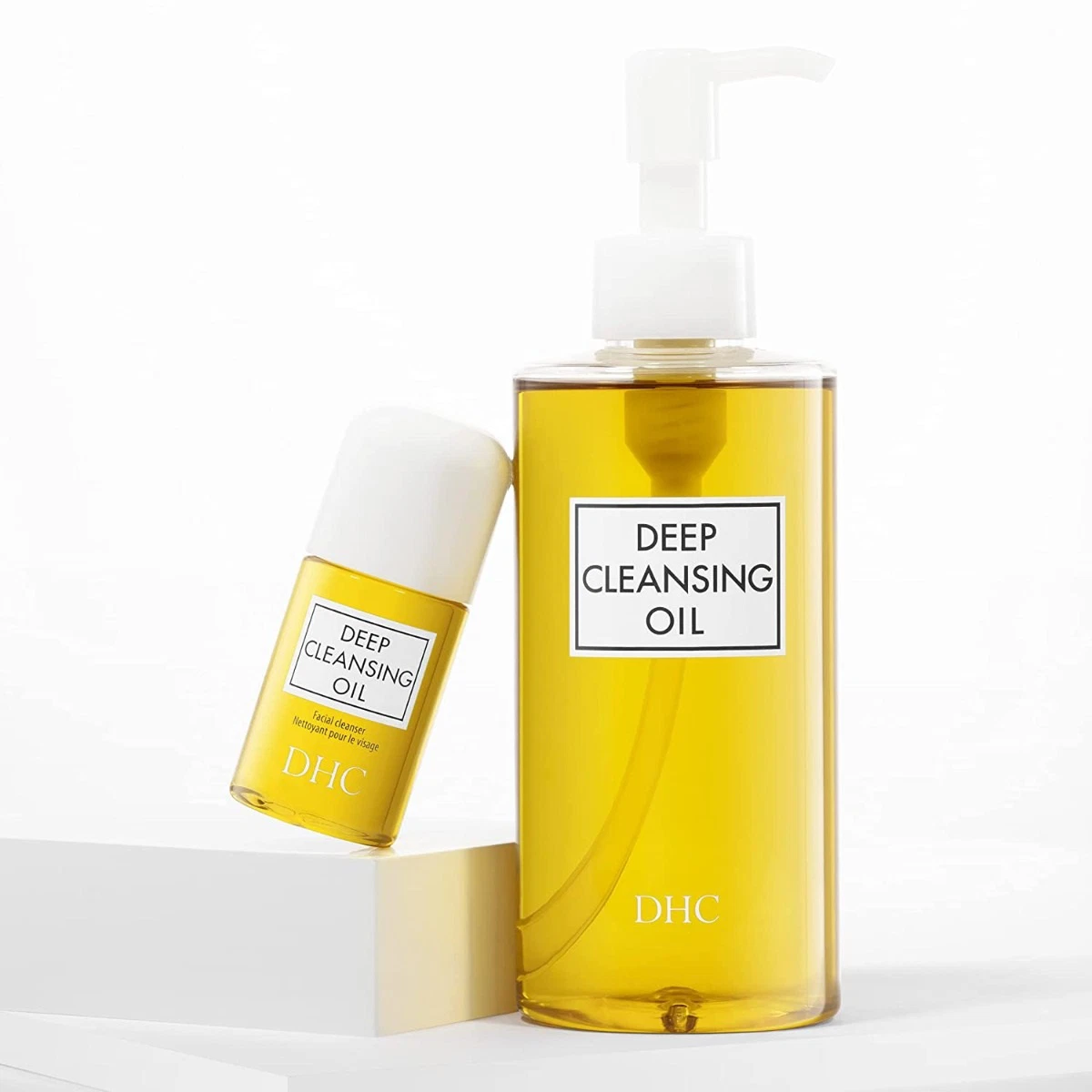 Hai chai dầu tẩy trang màu vàng, nhãn "Deep Cleansing Oil", đặt trên bề mặt trắng.