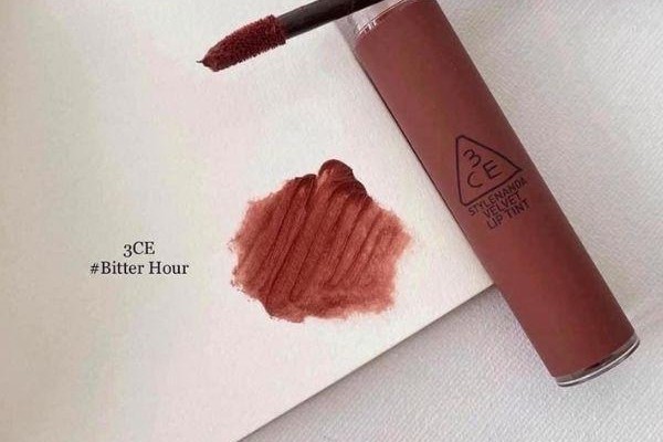 Son kem màu nâu đỏ với thân chai và cọ, đang được thử trên bề mặt trắng.