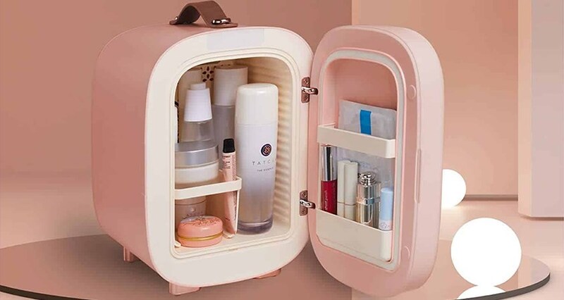 Tủ lạnh mini màu hồng chứa mỹ phẩm, bao gồm chai lọ và son môi, được đặt trên nền màu nâu nhạt.