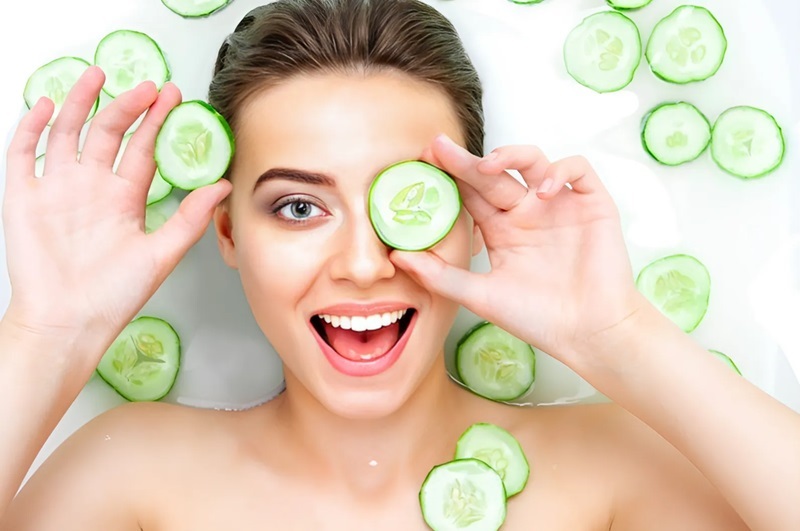 Người phụ nữ thư giãn trong bồn tắm, đặt lát dưa chuột lên mặt và xung quanh người.