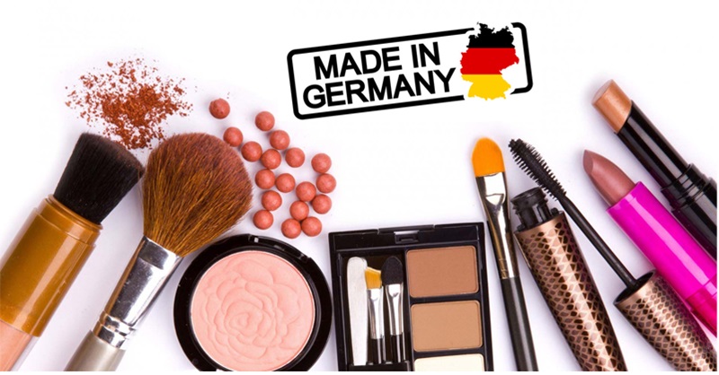 Bộ sưu tập mỹ phẩm và cọ trang điểm kèm nhãn "Made in Germany" trên nền trắng.