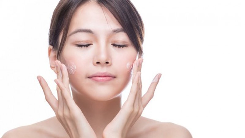 Người phụ nữ đang thoa kem dưỡng da lên mặt với phông nền trắng.