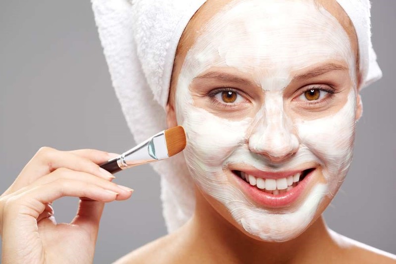 Người đắp mặt nạ trắng lên mặt, dùng cọ, quấn khăn trên đầu, cười nhẹ nhàng.