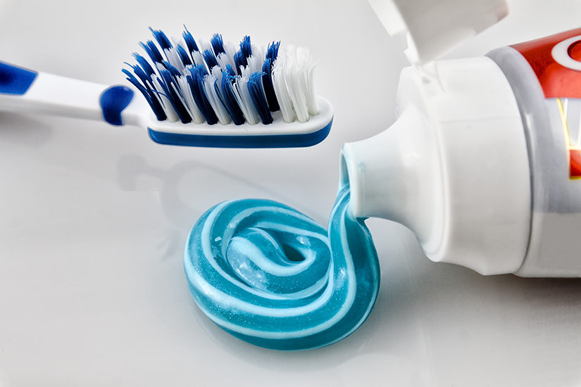 Bàn chải đánh răng và kem đánh răng màu xanh được nặn ra từ một tuýp đang mở nắp.