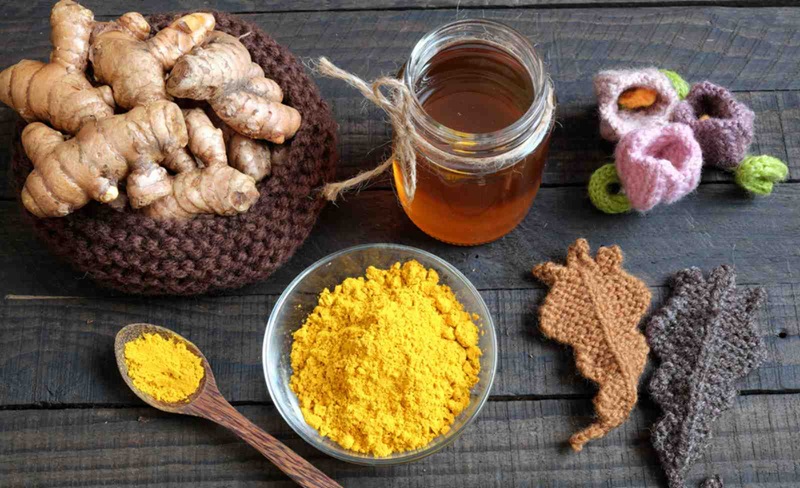 Củ nghệ tươi, bột nghệ, hũ mật ong và đồ trang trí len trên bàn gỗ.