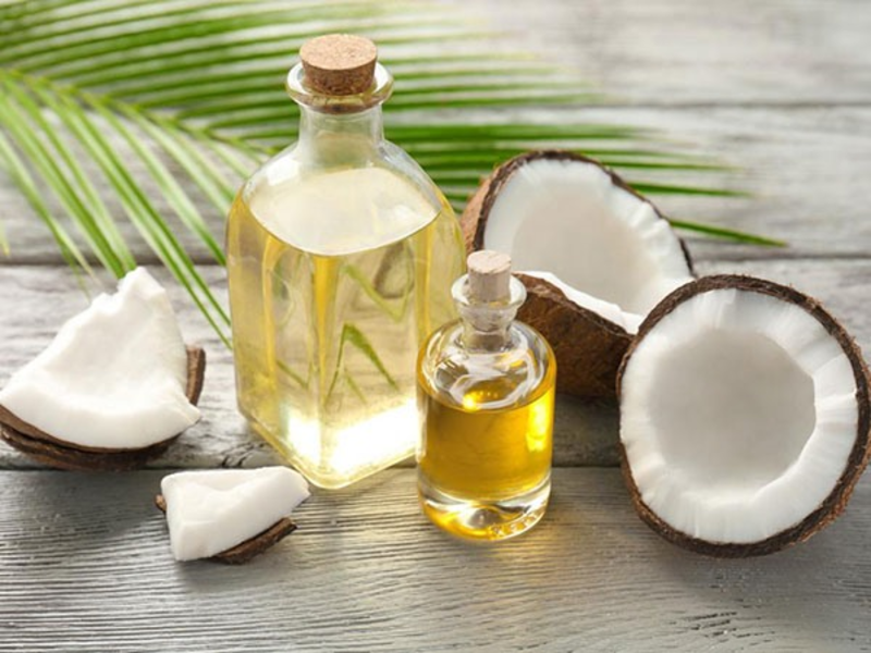 Hai chai dầu dừa trên bàn gỗ với nửa quả dừa và lá dừa ở phía sau.