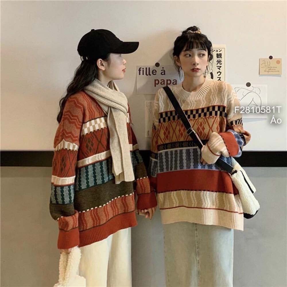 Hai người mặc áo len họa tiết đứng cạnh nhau, một người đeo khăn quàng, người kia mang túi xách.