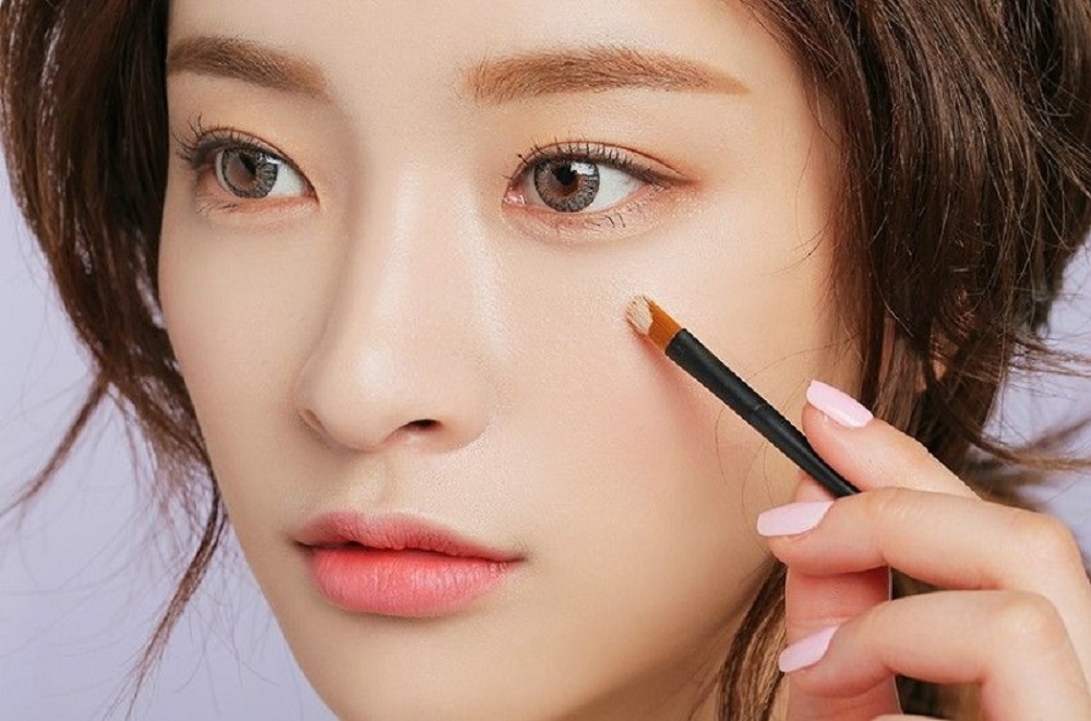 Kem Che Khuyết Điểm Tốt Nhất Cho Da Mụn: Lựa Chọn Hoàn Hảo Cho Bạn Gái 3 Người cầm cọ trang điểm gần vùng mắt, nền da sáng, tóc nâu.