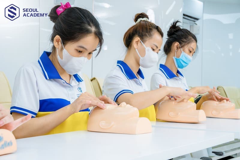 Học viên thực hành trên mẫu giả khuôn mặt trong lớp học tại một học viện, mặc đồng phục và đeo khẩu trang.