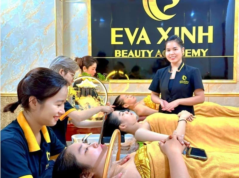 Nhân viên thẩm mỹ viện đang chăm sóc khách hàng trong một phòng dịch vụ, với bảng hiệu thương hiệu phía sau.